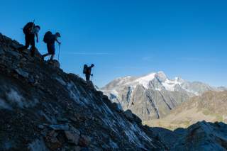Bergsteigergruppe steigt über die Gletscherreste des Bertolgletschers ab. Im Hintergrund leuchtet der vergletscherte Pigne d'Arolla.